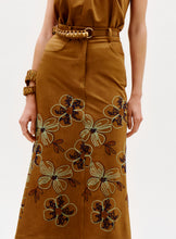 Load image into Gallery viewer, Wearing the Layan Skirt, a brown skirt with large embroidered floral patterns, paired with a matching brown top and accessorized with a chunky brown belt and bracelet.