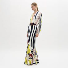 Load image into Gallery viewer, A woman stands wearing the Florina Skirt, a long, flowing piece with vertical and diagonal stripes in black, yellow, and red.