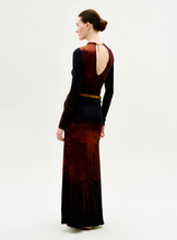 Load image into Gallery viewer, A woman with her hair in a neat bun stands against a plain white background, wearing the Gabbice Dress—a long-sleeved black and red patterned dress featuring an open back and a belt.