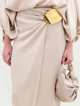 Load image into Gallery viewer, A woman stands against a white background wearing the beige Adrianne Skirt with an off-the-shoulder hammered satin top, a gold-tone embellishment belt, gold heels, and carrying a matching beige handbag.