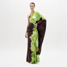 Load image into Gallery viewer, A person models the Afrodita Dress—a one-shoulder, floor-length gown with a green and brown tie-dye print—paired with gold necklaces, against a plain white background.