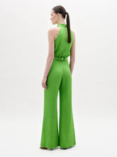 Load image into Gallery viewer, A woman stands facing forward in the Siv Jumpsuit, a bright green halter-neck style with wide-leg pants and a matching belt, paired with black sandals, against a plain white background.