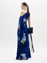 Load image into Gallery viewer, A woman stands against a plain background wearing the Dotty Dress, a one-shoulder blue dress with a yellow and white floral pattern, and holds a black clutch with a fringe strap.