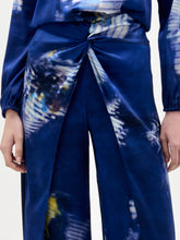 Load image into Gallery viewer, A person stands against a white background wearing the Canturipe Pant, paired with a blue patterned satin blouse and a choker-style scarf.