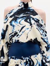 Load image into Gallery viewer, A woman stands against a plain background wearing the Safira Blouse, a high-neck, cold-shoulder top with matching wide-leg pants in a blue, black, and white marble pattern.