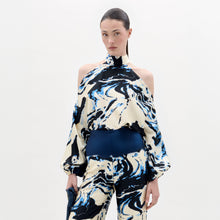 Load image into Gallery viewer, A woman stands against a plain background wearing the Safira Blouse, a high-neck, cold-shoulder top with matching wide-leg pants in a blue, black, and white marble pattern.