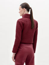 Load image into Gallery viewer, A woman stands against a plain background wearing the Zalta Jacket, a textured red jacket paired with a striped shirt, red pants, and a large black belt featuring an ornate buckle.