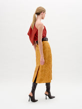 Load image into Gallery viewer, A woman models the Layan Skirt—a mustard yellow structured skirt with a large circular belt—styled with a red blouse and black heeled boots against a plain white background.