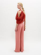 Load image into Gallery viewer, A woman stands in high-waisted pink Palermo Pants, crafted from luxurious Italian fabric, paired with a red one-shoulder top, gold belt, gold bracelets, and open-toe shoes against a white background.