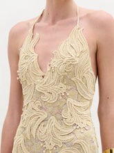 Load image into Gallery viewer, A woman wears the Aurora Dress—floor-length, sleeveless, crafted from gold lace with a fitted silhouette and wavy patterns—paired with gold cuff bracelets, standing against a plain white background.