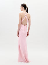 Load image into Gallery viewer, A person stands facing forward wearing the Daniela Dress Pink—a long, pastel pink dress featuring a halter neck and a large rose embellishment at the front. The background is plain white. Available for pre-order now, the dress will ship by February 1st, 2025.