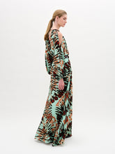 Load image into Gallery viewer, A woman wears the Carla Dress, a long patterned maxi with cut-out shoulders, a gathered neckline, long sleeves, a wide belt, and crafted from luxurious Italian fabric, standing against a plain white background.