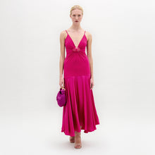 Load image into Gallery viewer, A woman poses against a white background in the Casiana Dress, a bright pink midi style made from Italian fabric with a deep V neckline. She pairs it with a matching small handbag and nude heels.