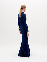 Load image into Gallery viewer, A woman wearing the Florina Skirt—a floor-length navy blue skirt with a mermaid silhouette and gathered knot detail at the waist—paired with gold jewelry, stands against a plain white background.