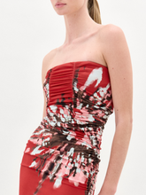 Load image into Gallery viewer, A woman wears the Collins Dress, a strapless maxi made from Italian fabric, with a fitted bodice and abstract white, pink, and black floral patterns on the skirt and waist.