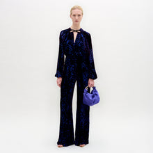 Load image into Gallery viewer, A woman wearing the Como Pant in color Eggplant Velvet with a Sofia bag in color Spectrum blue on a white background