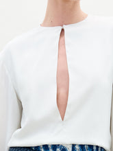 Load image into Gallery viewer, A woman poses against a plain background wearing the Covilha Blouse, featuring a keyhole neckline and balloon sleeves, styled with high-waisted blue patterned pants and holding a small beige bag.