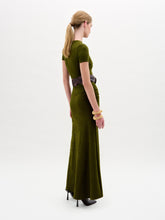 Load image into Gallery viewer, A woman wearing the Cristal Dress, an olive green slim fit maxi dress paired with a wide black belt with a gold buckle, black boots, and gold bracelets stands against a plain white background.