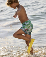 Load image into Gallery viewer, Boy playing in water wearing floral swim shorts and yellow shoes.