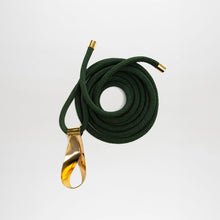 Load image into Gallery viewer, The Daiana Belt is a coiled dark green cord with gold metal caps and a large gold-plated brass buckle, crafted from fine Italian material and shown on a plain white background.