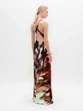 Load image into Gallery viewer, A woman stands against a plain white background wearing the Daniella Dress—a sleeveless maxi with a deep V-neckline, featuring a light blue top and a brown and red abstract print on the lower half.