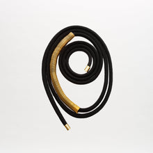Load image into Gallery viewer, The Dunia Belt, crafted from fine Italian material, features a coiled black cord with gold-capped ends and striking gold accents, artfully arranged in a spiral on a plain white background.
