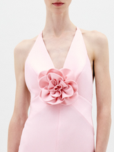Load image into Gallery viewer, A person stands facing forward wearing the Daniela Dress Pink—a long, pastel pink dress featuring a halter neck and a large rose embellishment at the front. The background is plain white. Available for pre-order now, the dress will ship by February 1st, 2025.