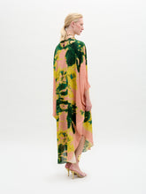Load image into Gallery viewer, A woman stands against a white background wearing the Elea Tunic, an oversized 100% silk maxi dress with pink, yellow, and green patterns, paired with a beige bag and strappy heels.