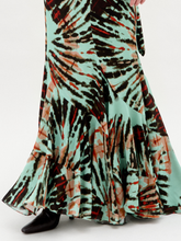 Load image into Gallery viewer, Against a plain white background, a person wears the Florina Skirt, crafted from luxurious Italian fabric. This long skirt showcases a vibrant tie-dye pattern with green, orange, and black hues cascading elegantly down its maxi length.