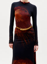 Load image into Gallery viewer, A person in the Gabbice Dress—a long-sleeved, fitted black dress with abstract red and brown patterns—paired with a chunky gold necklace and a gold belt worn diagonally, stands against a plain light background.