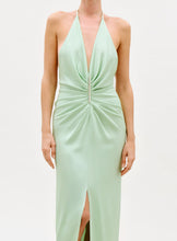 Load image into Gallery viewer, A woman stands against a white background wearing the Jenifer Dress, a sleeveless light green halter-neck design featuring a deep V-neckline, gathered waist, and front slit.