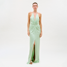Load image into Gallery viewer, A person stands against a plain white background wearing the Jenifer Dress, a light green sleeveless evening gown featuring a halter neckline, gathered front detail, and a high front slit.