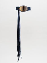 Load image into Gallery viewer, The Kai Belt is a black braided belt with a large oval gold buckle and long black fringe hanging down one side, shown on a plain light grey background.