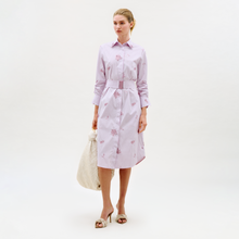 Load image into Gallery viewer, A woman wears the Kendi Dress—a long-sleeve, belted shirt dress with light pink and white stripes and floral patterns—paired with a quilted white bag and heeled sandals against a plain background.