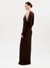 Load image into Gallery viewer, A woman in profile wears the Kilian Dress—a long, dark brown gown with draped and open shoulder details. Her hair is neatly pulled back in a bun as she poses against a simple, light background.