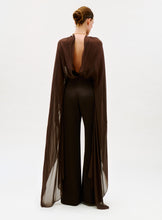 Load image into Gallery viewer, A person stands facing away, wearing the Ligia Jumpsuit—a sheer, flowing brown design with matching wide-leg pants and an open back—styled with a neat updo against a plain light background.