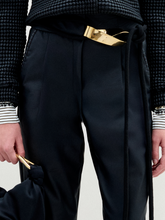 Load image into Gallery viewer, Person stands against a plain white background wearing the Moad Pant, a dark textured jacket, patterned shirt, black boots, and holding a small black handbag.