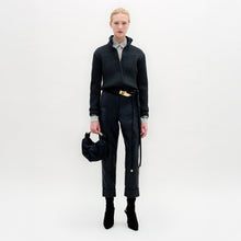 Load image into Gallery viewer, Person stands against a plain white background wearing the Moad Pant, a dark textured jacket, patterned shirt, black boots, and holding a small black handbag.