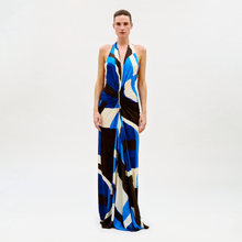 Load image into Gallery viewer, A person poses against a plain light background wearing the Malek Dress, a long halter-neck style with a bold blue, black, white, and beige geometric pattern and a knotted waist detail.