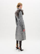 Load image into Gallery viewer, A woman stands against a plain background wearing the Nilo Trench, a textured gray structured coat with a large floral shoulder detail, paired with black heeled boots and a gold ankle accessory.