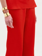 Load image into Gallery viewer, A woman poses against a white background in the sleeveless red halter top and high-waisted, wide-leg Palermo Pant in hammered satin, accessorized with gold bracelets.