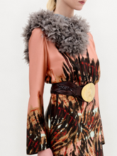 Load image into Gallery viewer, A person stands in profile wearing the Pesaro Dress—a peach silk midi with a large feathered design, wide belt with round buckle, gray fur collar, and black heeled boots—set against a plain background.