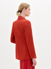Load image into Gallery viewer, A person wearing the Rebeca Jacket, a fitted red blazer made from Italian fabric, layered over a patterned red and beige dress, stands against a plain light background.
