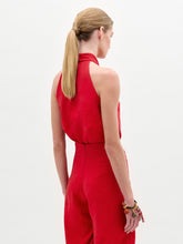 Load image into Gallery viewer, Woman wearing the Shela Blouse, a sleeveless red halter-neck top made from Italian fabric with a knotted front detail, standing against a plain light background.