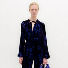 Load image into Gallery viewer, A woman wearing the Ximena Blouse in color Eggplant Velvet with a Sofia bag in color Spectrum blue on a white background