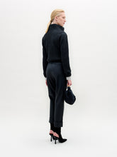 Load image into Gallery viewer, A person stands against a plain white background wearing the Zalta Jacket, a dark cropped piece crafted from Italian fabric, paired with a striped shirt, dark trousers with a gold belt, and holding a dark bag.