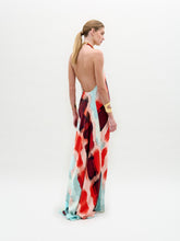 Load image into Gallery viewer, A woman poses against a white background wearing the Zeffa Dress, a sleeveless, floor-length silk maxi with an abstract red, aqua, and white pattern, paired with gold jewelry.
