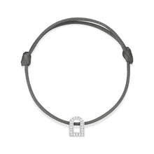 Load image into Gallery viewer, Introducing the L'Arc Voyage Charm PM: a minimalist bracelet crafted in 18k white gold with Galerie diamonds. It features a slender gray silk cord with an adjustable knot, embodying the Paris Atelier style, and is adorned with a lock-shaped charm encrusted with small sparkling stones resembling diamonds.