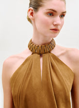 Load image into Gallery viewer, A woman with light skin and blue eyes, her hair slicked back neatly, wears the Ann Blouse—a tan halter style with a high, wide textured collar—while looking slightly to the side against a plain light background.
