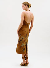 Load image into Gallery viewer, A woman stands in profile, wearing the Layan Skirt with a tan, floral design. She pairs it with matching high-heeled sandals and wears her hair in a neat bun, posing against a simple light background.
